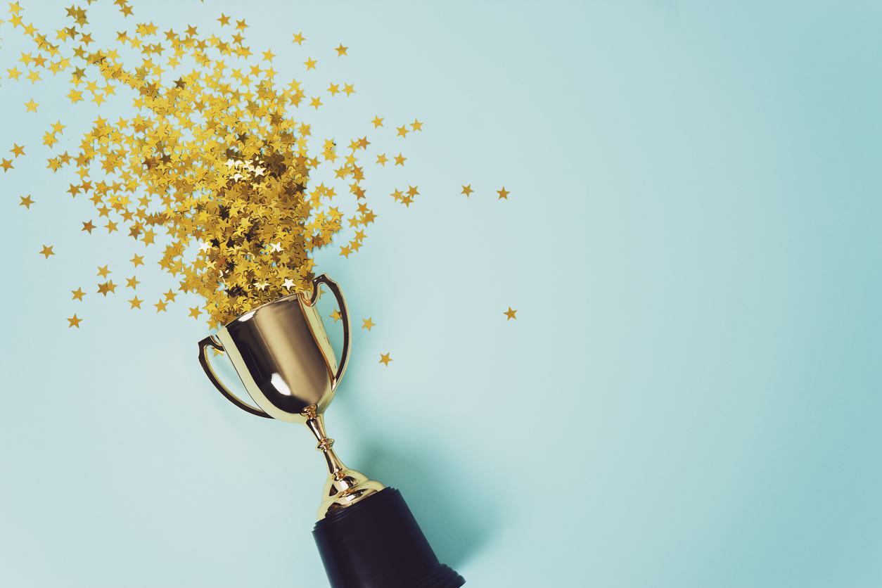 A gold trophy spilling golden star confetti on a light blue background, symbolizing excellence and achievement.